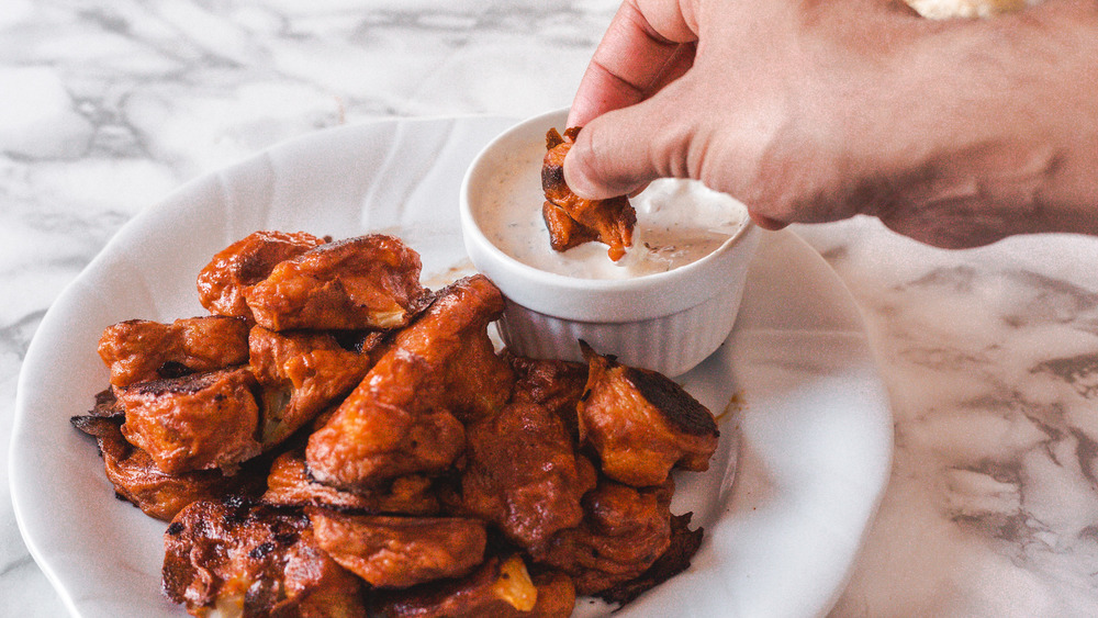 hand dipping buffalo cauliflower into sauce