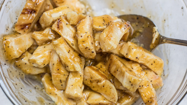 Close up of a metal spoon stirring chicken strips covered in teriyaki sauce