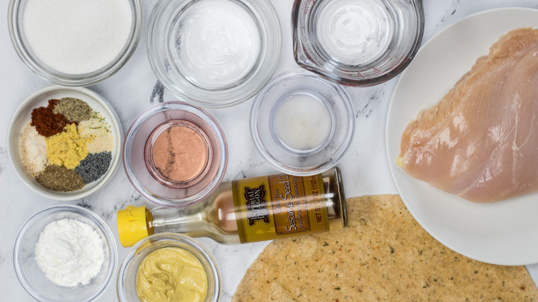 Raw chicken breast on a white plate next to liquid and powder ingredients