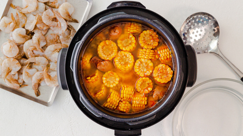 An Instant Pot filled with corn and sausage next to a tray of shrimp