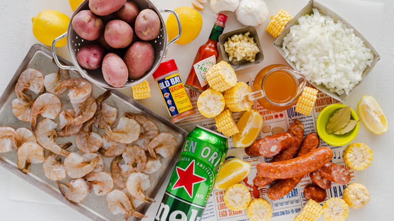 Shrimp, potatoes, rice, corn seasoning, beer, sausage, garlic, and lemons scattered across a table