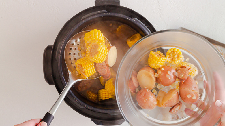 Closeup of someone removing corn, sausage, and potatoes from an Instant Pot