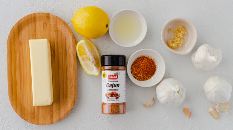 A stick of butter on a wooden butter dish next to lemons, spice, and garlic