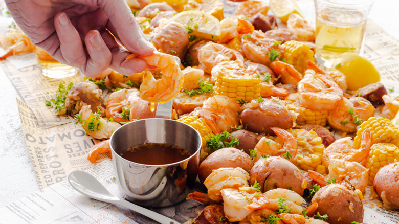 Close up Instant Pot Shrimp Boil and a hand dipping shrimp in seasoned butter