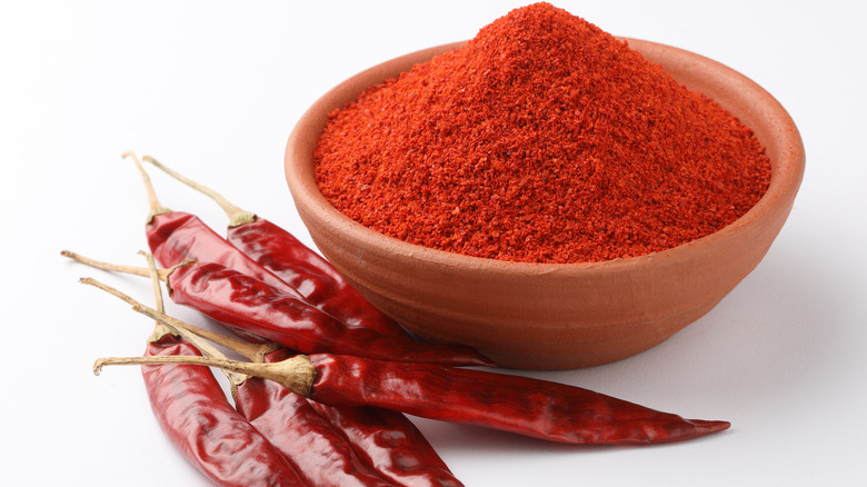 Bowl of paprika with cayenne peppers beside it