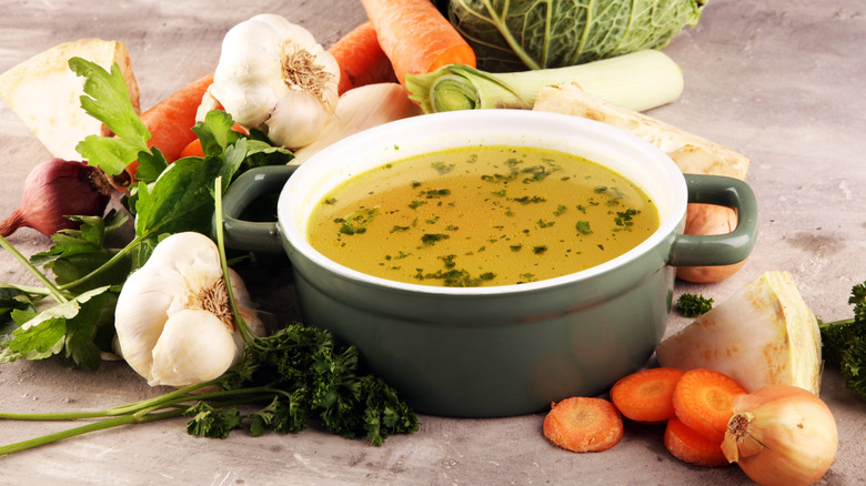 A pot of vegetable broth surrounded by vegetables