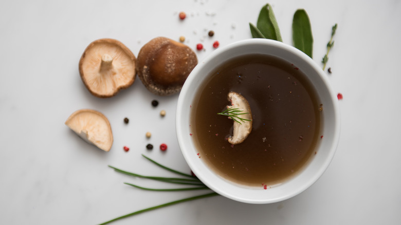 A bowl of mushroom broth on top of sprigs of leaves