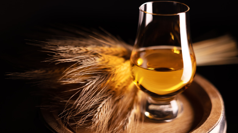 a glass of bourbon on barrel with wheat