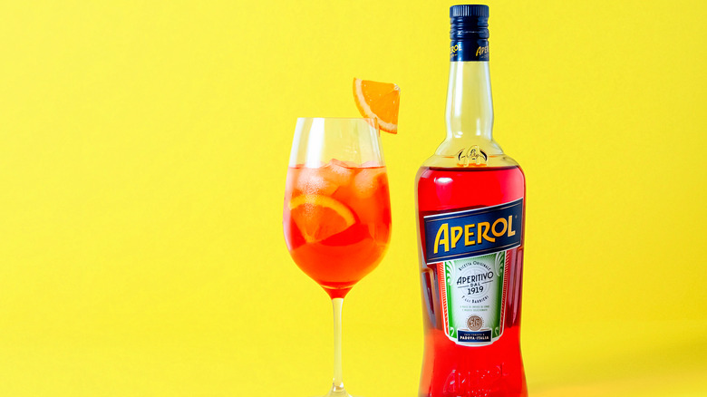 A bottle of Aperol next to a cocktail on a yellow background