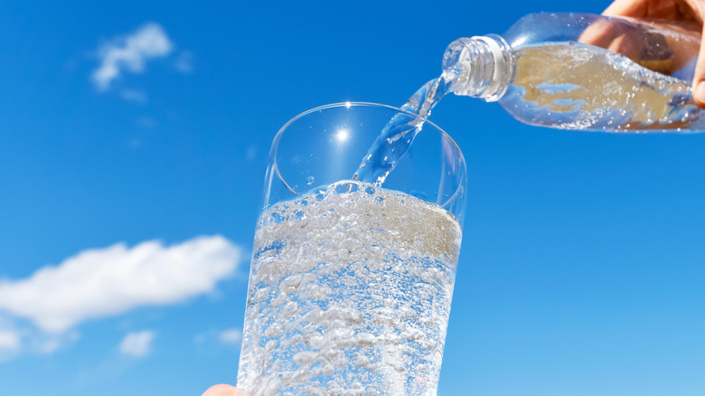 Person pouring seltzer water into a glass with blue sky in background