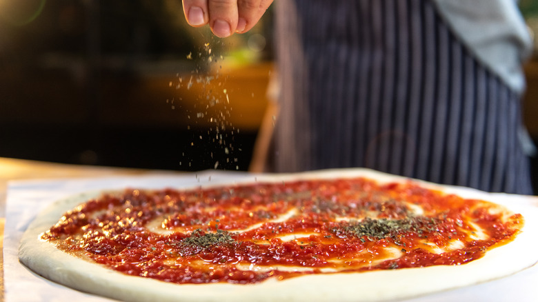 Hand sprinkling seasoning over pizza