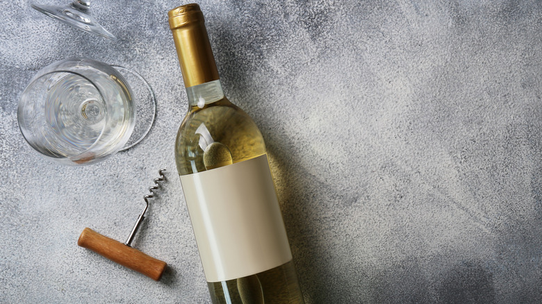 A bottle of white wine with a glass and corkscrew on silver background