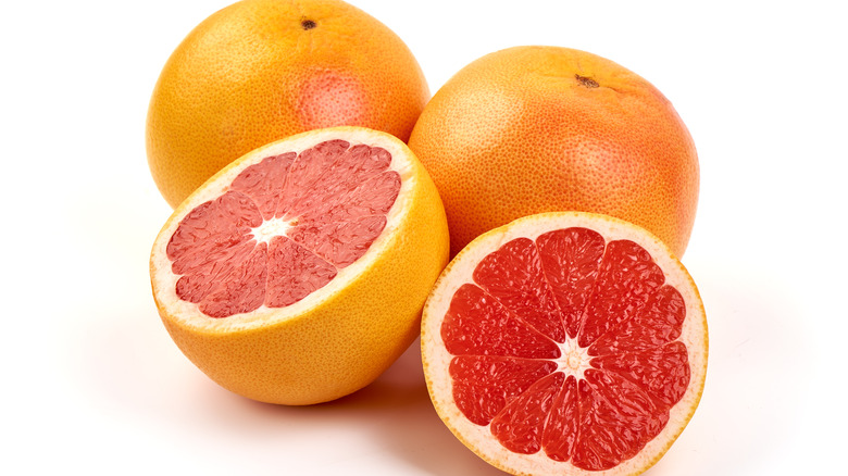 Two whole grapefruit and one cut in half on white background