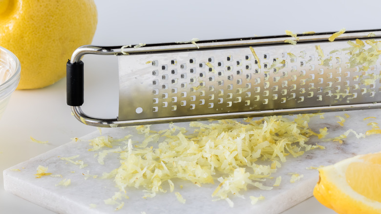 A grater with lemon zest on a cutting board and lemon in background