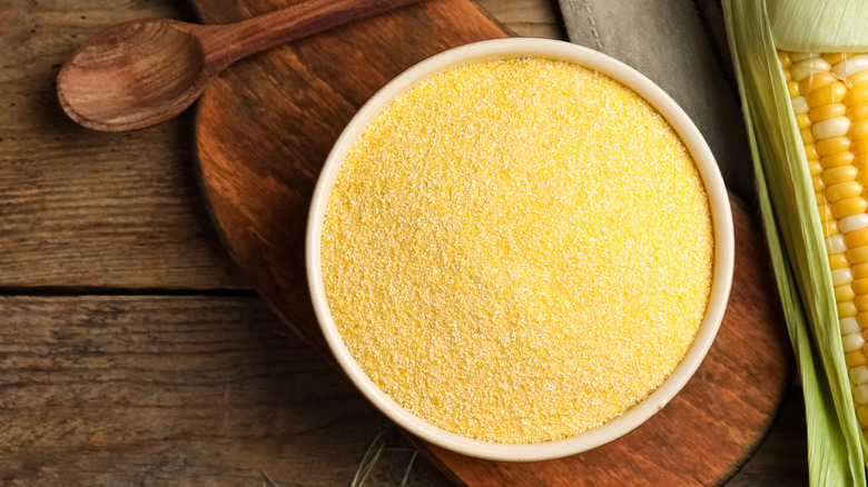 ground cornmeal on wooden table next to wooden spoon