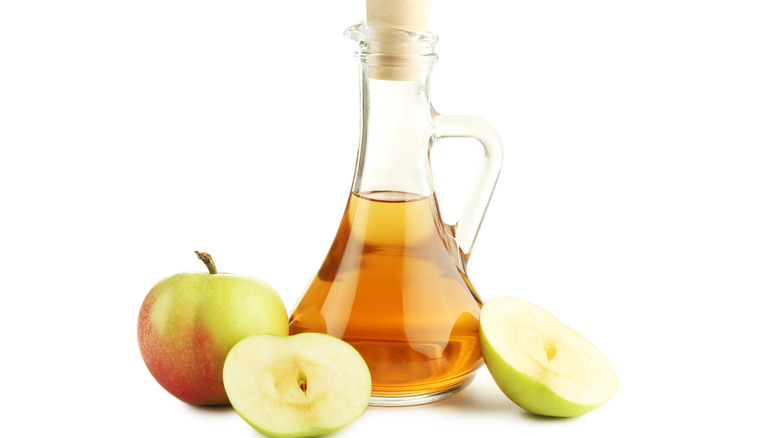 Bottle of apple cider vinegar surrounded by apples