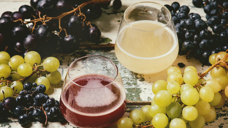 Glasses of juice next to white and red grapes