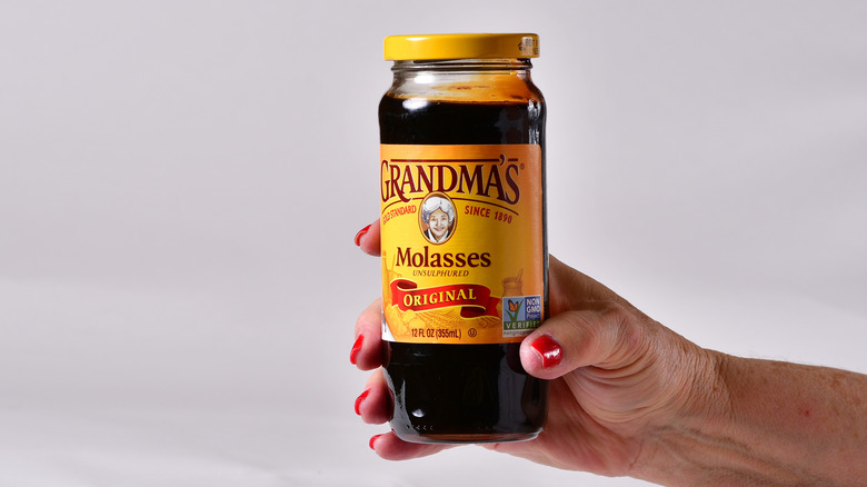 A hand holding a jar of molasses