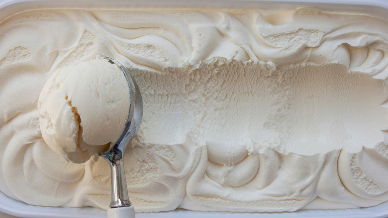 A close up of a hand scooping vanilla ice cream