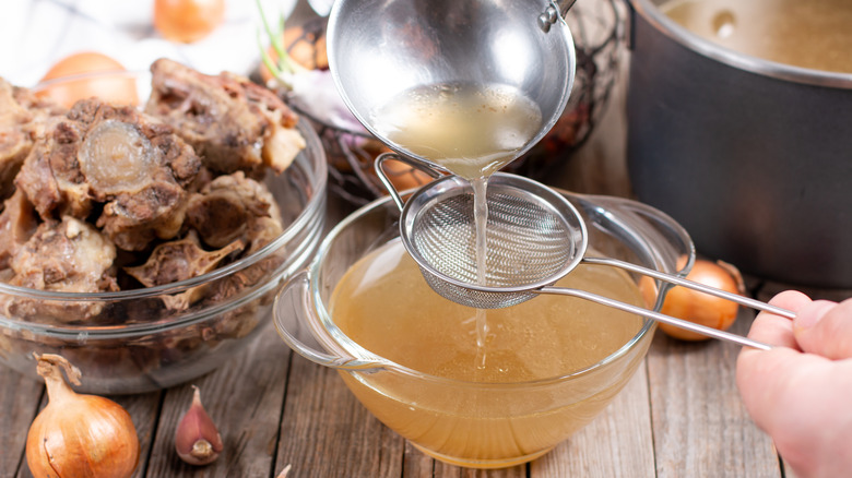 A person straining beef broth in a bowl