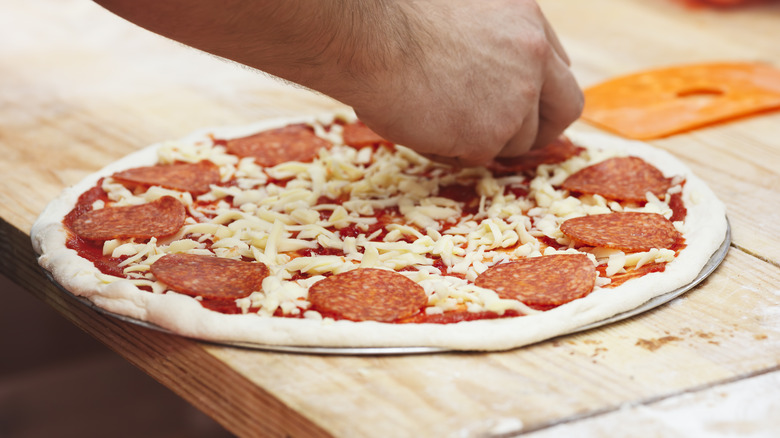 Person preparing uncooked pizza