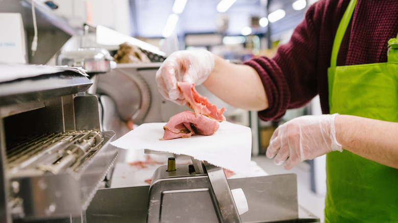 A worker assembles slices of meat on a scale in a deli.