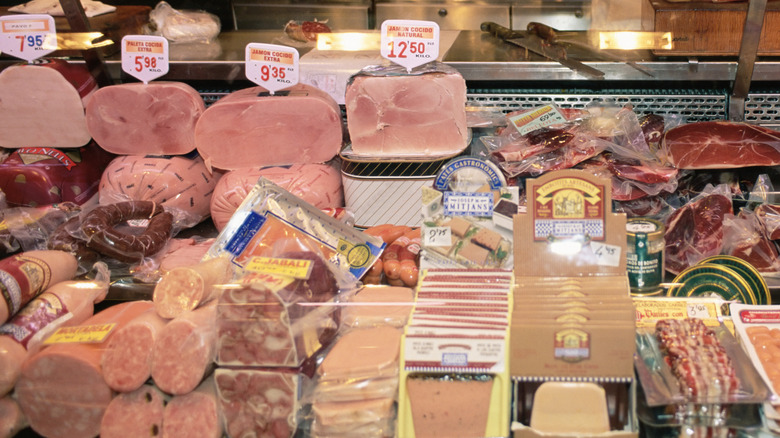 Assorted meats sit in a refrigerated deli case.