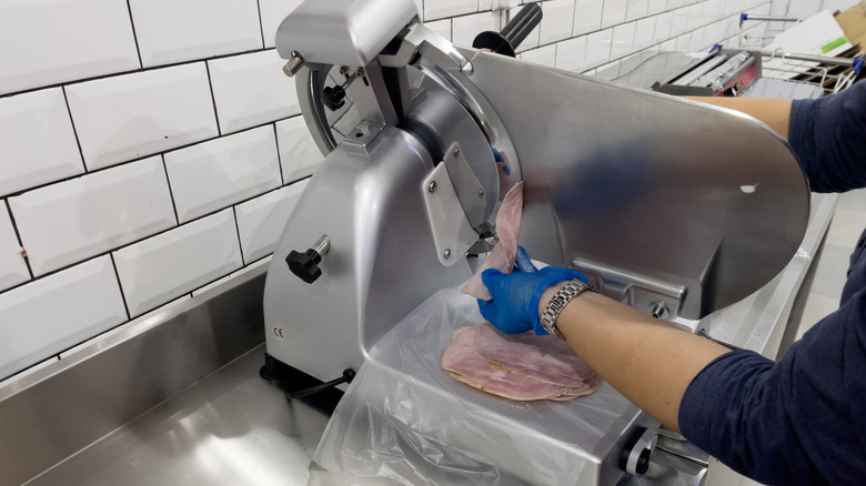 A worker uses a slicer for meat.