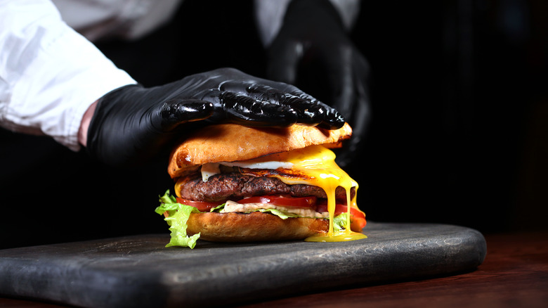 Chef in black gloves cooking a hamburger.