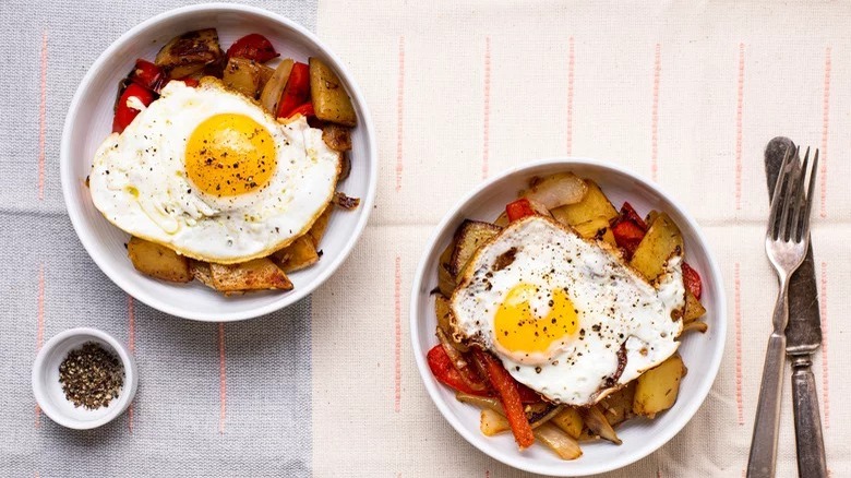 bowls of veggie breakfast hash with sunny side up eggs fork and knife