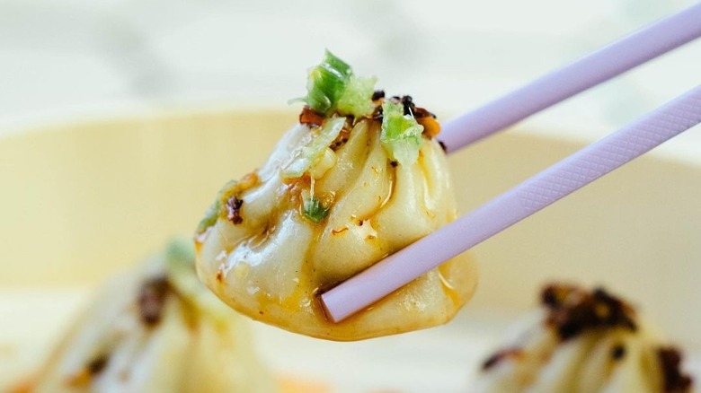 A soup dumpling topped with chili crisp held by chopsticks.