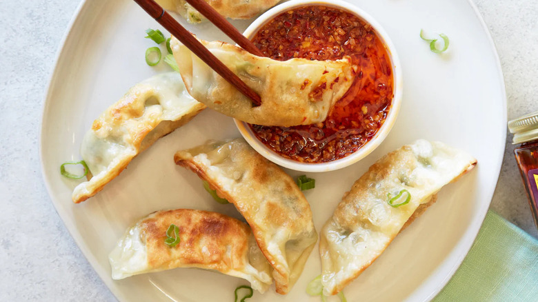 A white plate of Trader Joe's potstickers with chili sauce and scallions.