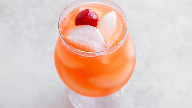 Cocktail glass with pink-orange drink on ice. 