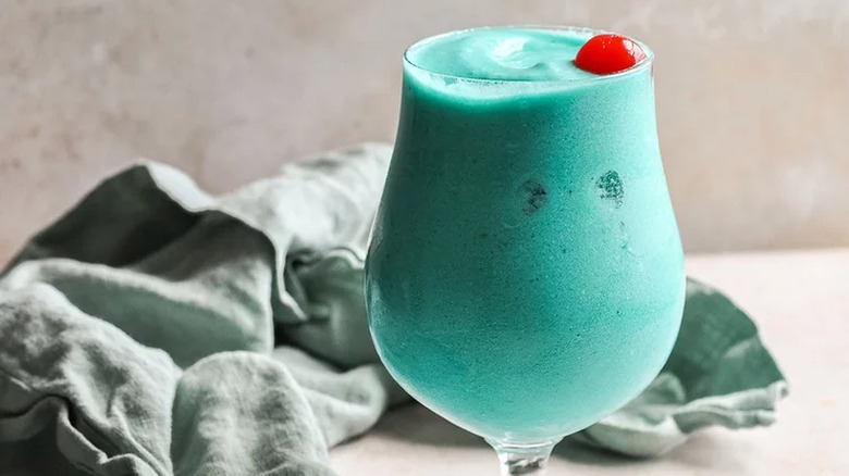 Frozen blue cocktail in glass with red cherry.