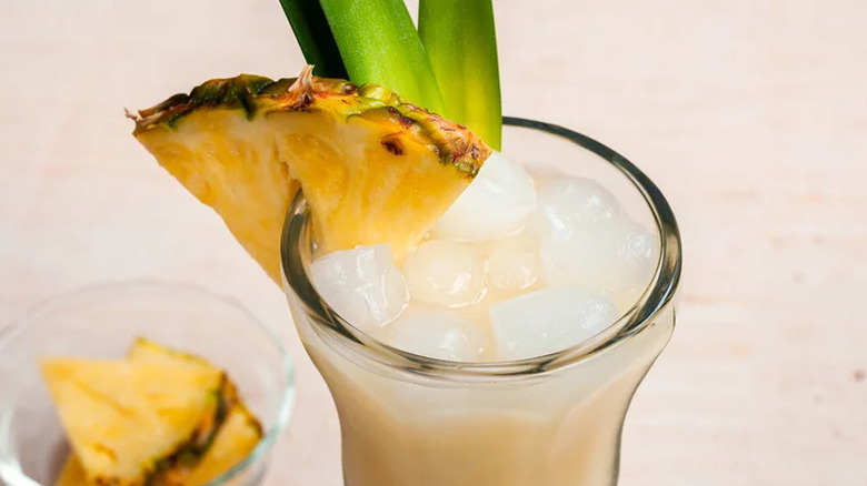 Tall glass with ice, creamy cocktail, and pineapple wedges.