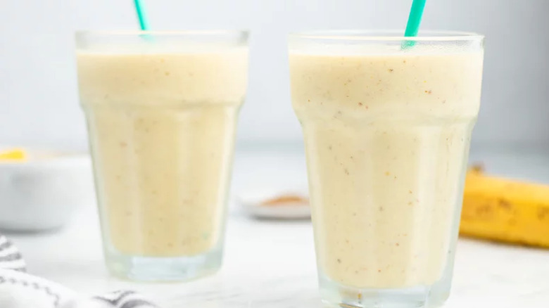 Pale yellow smoothies in glasses with straws.