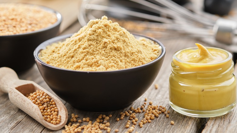 whole and ground mustard seeds beside small jar of mustard