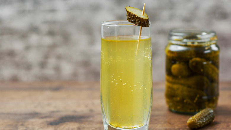 glass of pickle juice with pickle slice garnish in front of jar of pickles