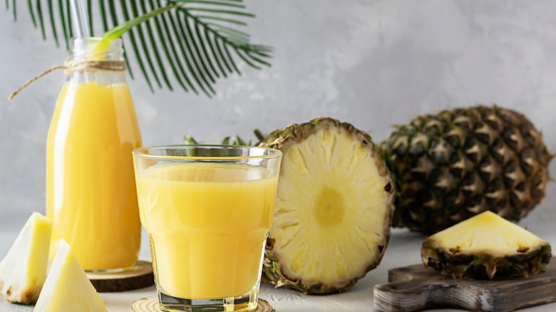 Cut pineapple beside bottle and glass of pineapple juice