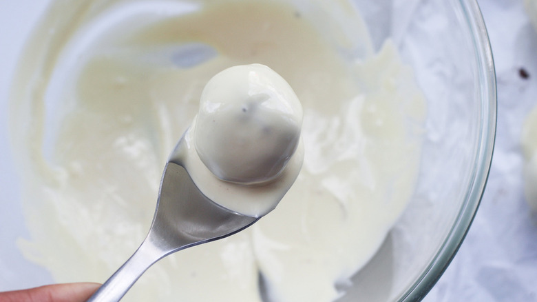 Close up of a metal spoon holding a white chocolate coated Oreo truffle over a bowl of melted white chocolate