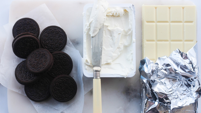 A pile of Oreos next to a tub of cream cheese, which is next to a bar of white chocolate