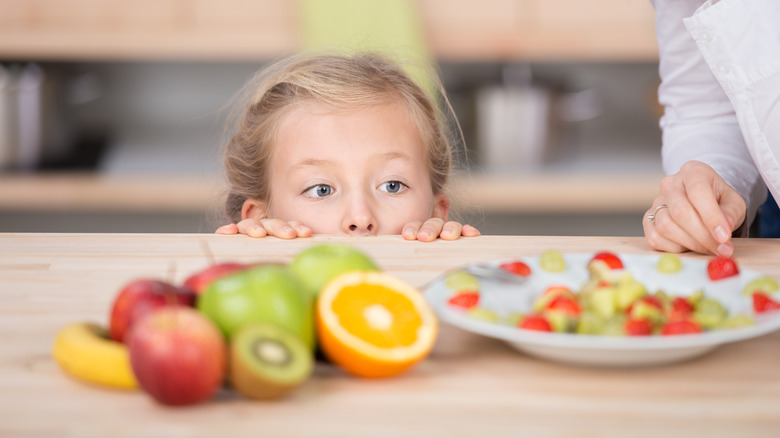 child looking over counter at fruit plate with woman