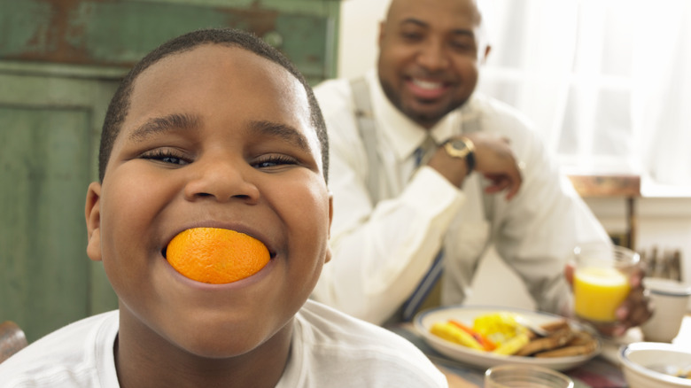 happy child eating orange segment with man in background