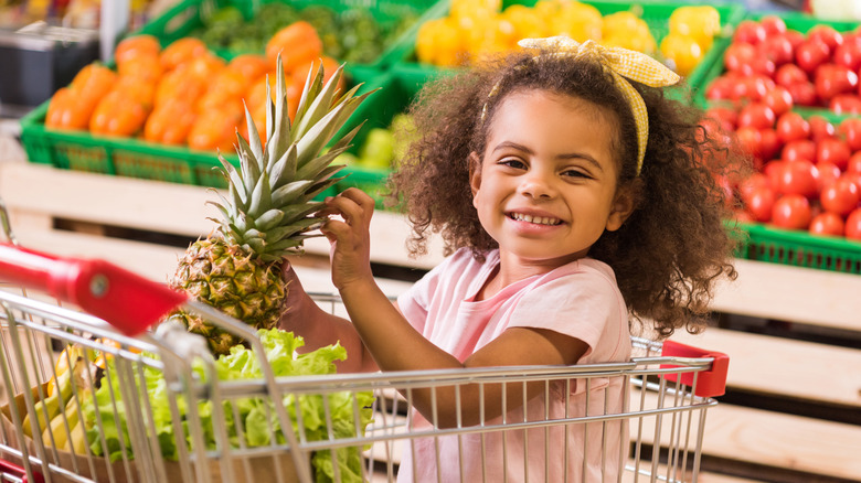 child in shopping cart with groceries