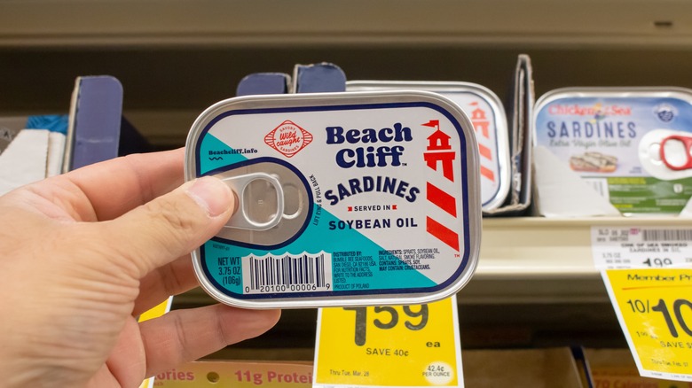 hand holding can of sardines in supermarket