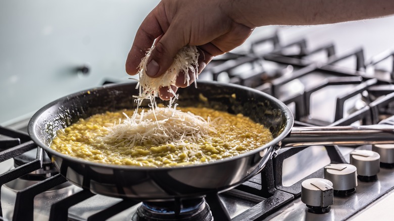 Hand adding Parmesan to risotto cooking on a stovetop