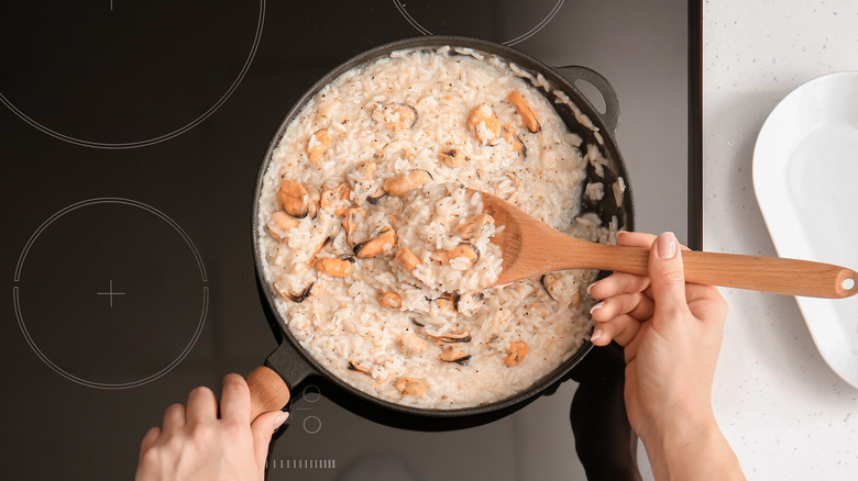 Hands stirring a risotto being prepared on a stovetop