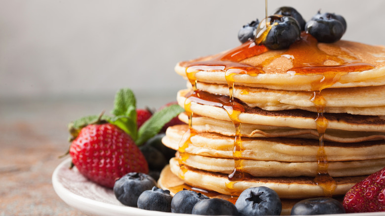 pouring syrup on stack of pancakes