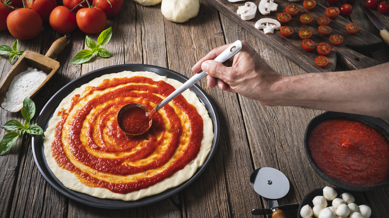 tomato sauce being spread on pizza