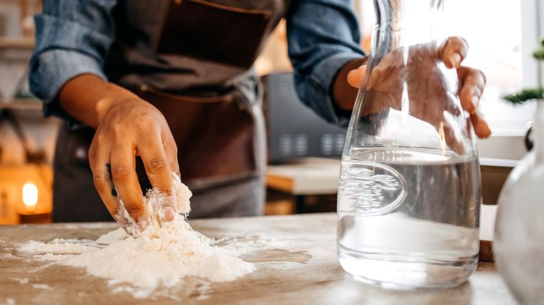 person making pizza dough on counter with large water jug